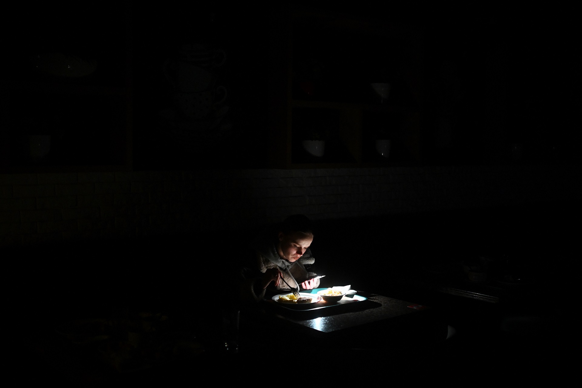 Sergei Gapon  AFP 21/11/2025
Una ragazza utilizza la torcia del suo smartphone per vedere il cibo nel piatto durante un blackout a Kiev, Ucraina. 